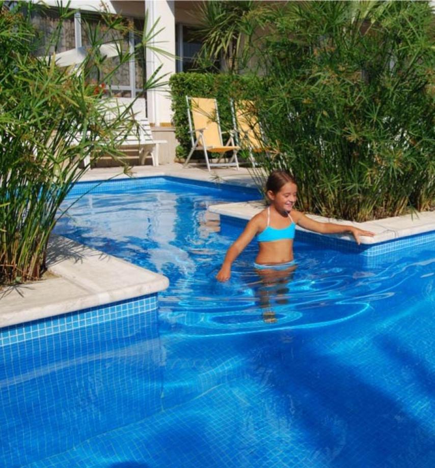 Bambina in piscina con piante verdi attorno.